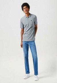 Szary polo z krótkim rękawem, z kołnierzykiem i trzema guzikami, w połączeniu z jasnoniebieskimi dżinsami i białymi sneakersami. Prosty design, bez wzorów.