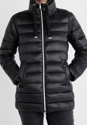 Czarna pikowana kurtka puchowa z poziomymi przeszyciami, wysokim kołnierzem, czarnymi sznurkami, przednim zamkiem błyskawicznym oraz dwoma zapinanymi na zamek bocznymi kieszeniami, noszona na ciemnych spodniach.