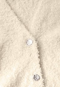 Weicher, weißer Cardigan aus strukturiertem Material mit flauschigem Stoff, einem V-Ausschnitt-Design und glänzenden, runden silbernen Knöpfen zum Schließen.