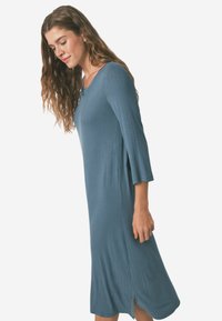 Abito a coste con maniche a tre quarti in un blu tenue, con scollatura a V e spacchi laterali per facilitare il movimento. Tessuto morbido e testurizzato.