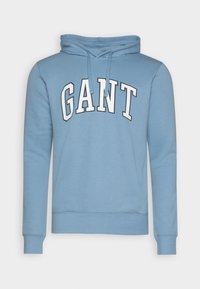 Felpa con cappuccio azzurro chiaro realizzata in tessuto morbido, con una grafica frontale che riporta "GANT" in bold bianco. Include un cappuccio con cordini.