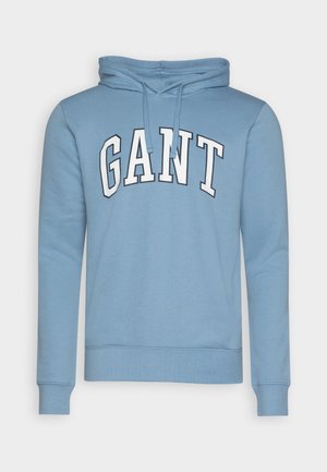 Moletom azul claro feito de tecido macio, apresentando uma estampa frontal com a palavra "GANT" em letras brancas em negrito. Inclui capuz com cordão.
