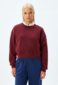 Burgundowe bluzy z ribbowanym dekoltem i mankietami, o luźnym kroju. W połączeniu z niebieskimi spodniami z elastyczną talią dla swobodnego wyglądu.