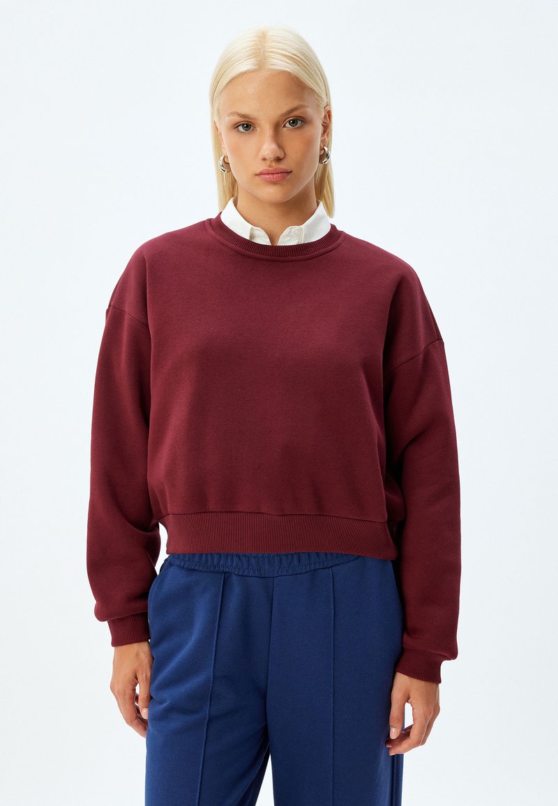 Burgundowe bluzy z ribbowanym dekoltem i mankietami, o luźnym kroju. W połączeniu z niebieskimi spodniami z elastyczną talią dla swobodnego wyglądu.
