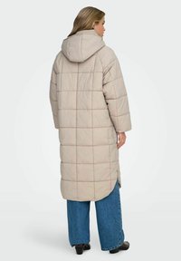 Beige, lång vadderad kappa med huva, med ett quiltat mönster. Matchas med vida jeans och ankelboots.