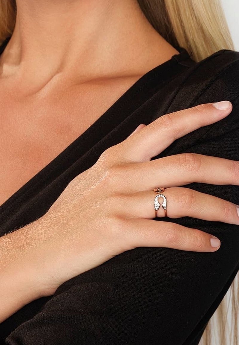 Gros plan sur la main d'une femme portant une bague en or rose avec un motif en forme de fer à cheval incrusté de diamants sur son doigt du milieu.