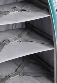 Szare wnętrze torby podróżnej z trzema przegródkami, zabezpieczone szarymi paskami i wyściełane materiałem w wzory oraz jasnoniebieskimi akcentami.