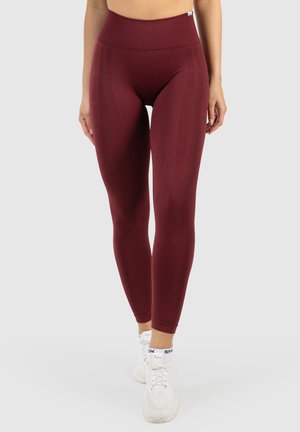 Burgunderfarbene Leggings mit hohem Bund, strukturiertem Stoff und dezentem Branding an den Seiten, kombiniert mit weißen Sportschuhen.
