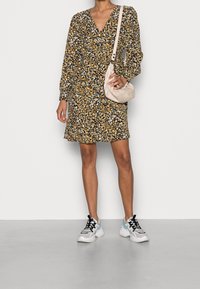 Vestito floreale con sfondo nero, fiori gialli e bianchi, scollo a V, maniche lunghe, abbinato a una borsa chiara e sneakers chunky.