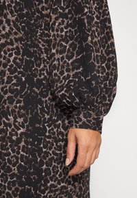 Robe à manches longues avec un imprimé léopard noir et marron. Tissu doux avec une surface texturée, manches bouffantes et coupe décontractée.
