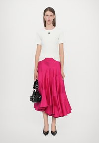 Un haut blanc à manches courtes avec un logo, associé à une jupe en satin rose à volants. Accessoirisé avec un petit sac à main noir et des talons pointus.