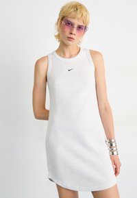 Grå ribbet tankkjole med rund hals og svart Nike-logo. Sølv armbånd på armen gir et metallisk preg.
