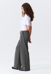 Pantalons amples gris à rayures, présentant une coupe cintrée, des poches avant et une taille haute, associés à un haut blanc à manches courtes.
