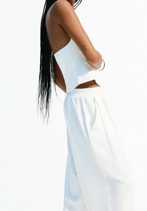 Witte cropped top met open rug, gecombineerd met losse witte broek. Licht, gladde stof met een ontspannen pasvorm en elastische tailleband.