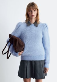 Helles blaues, flauschiges Sweater mit Puffärmeln, grauem Kragen und geripptem Saum. Grauer Faltenrock und braune Umhängetasche.