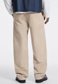Beige, loose-fitting pants with a smooth texture, featuring side pockets and a straight-leg design. The fabric appears lightweight.
