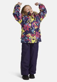 Färgglad blommönstrad pufferjacka med huva i päls, kombinerad med mörklila snöbyxor och svarta kängor.