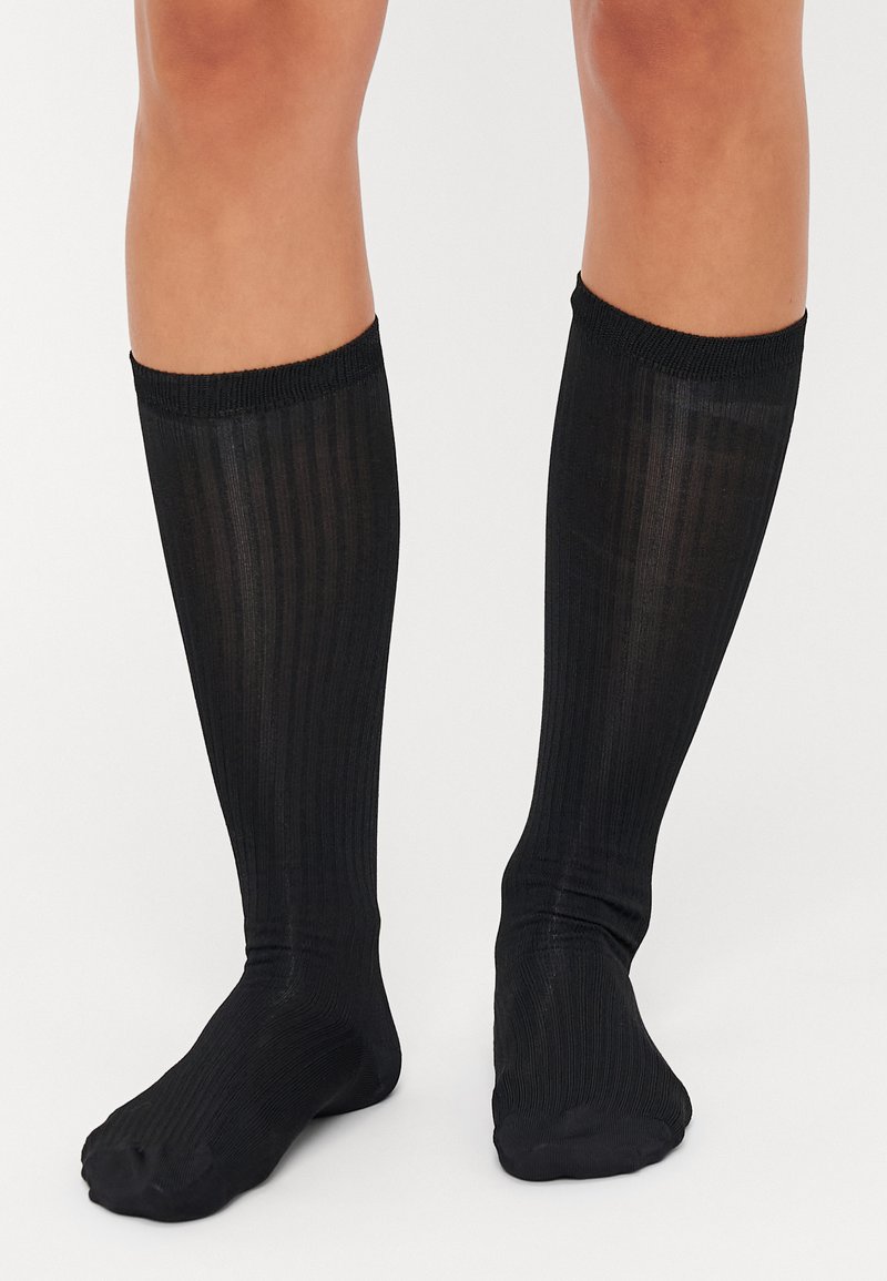 Chaussettes noires montantes avec une texture côtelée, orteils sans couture et un revers élastique doux en haut pour un maintien sécurisé.