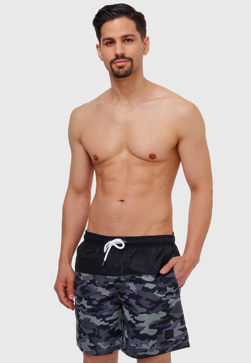 Shorts de bain en camouflage noir et gris avec une taille élastique et un cordon de serrage blanc, dotés de poches latérales et d'une texture lisse.
