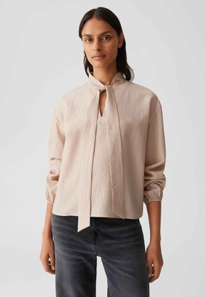 Hellbeige Bluse aus strukturierter Stoffqualität, mit hohem Kragen und Bindeband, langen Ärmeln mit elastischen Bündchen und einem Schlitzdetail.