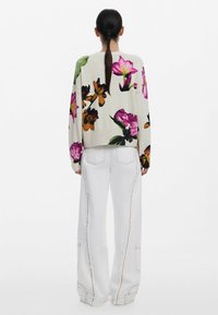 Floral-patterned sweater in cream with vibrant pink, orange, and green flowers; paired with loose-fitting white jeans featuring visible stitching.
