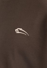 Brun bomulds t-shirt med en glat overflade, der har et hvidt broderet logo på venstre brystområde. Enkel, klassisk design og pasform.