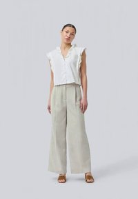 Blusa branca de botões, com mangas curtas e franzida, de corte solto, combinada com calças largas em xadrez bejes e sandálias castanhas.