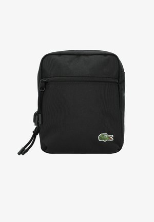 Sac en nylon noir avec une poche avant zippée, de forme rectangulaire, et un logo de crocodile brodé en vert dans le coin inférieur droit.