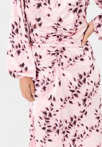 Langes pinkes Kleid mit einem gerafften Design und dunklen Blumenmustern. Der Stoff ist glatt und leicht glänzend, mit voluminösen Ärmeln.