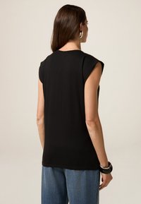 Top negro sin mangas con corte relajado, textura suave y escote redondo. Combinado con jeans de denim azul holgados y accesorios negros.