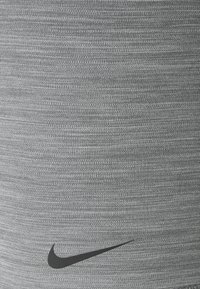 Gros plan sur un tissu tricoté gris clair avec le logo Nike swoosh noir dans la partie inférieure du textile.