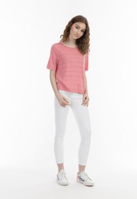 Pulover scurt roz cu mânecă scurtă, cu un model geometric texturat, combinat cu blugi albi, slim-fit, și adidași multicolori pe un fundal deschis.