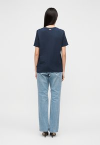 T-shirt azul-marinho de manga curta com decote redondo, combinada com jeans de perna reta azul-claro e sapatos pretos de salto alto.