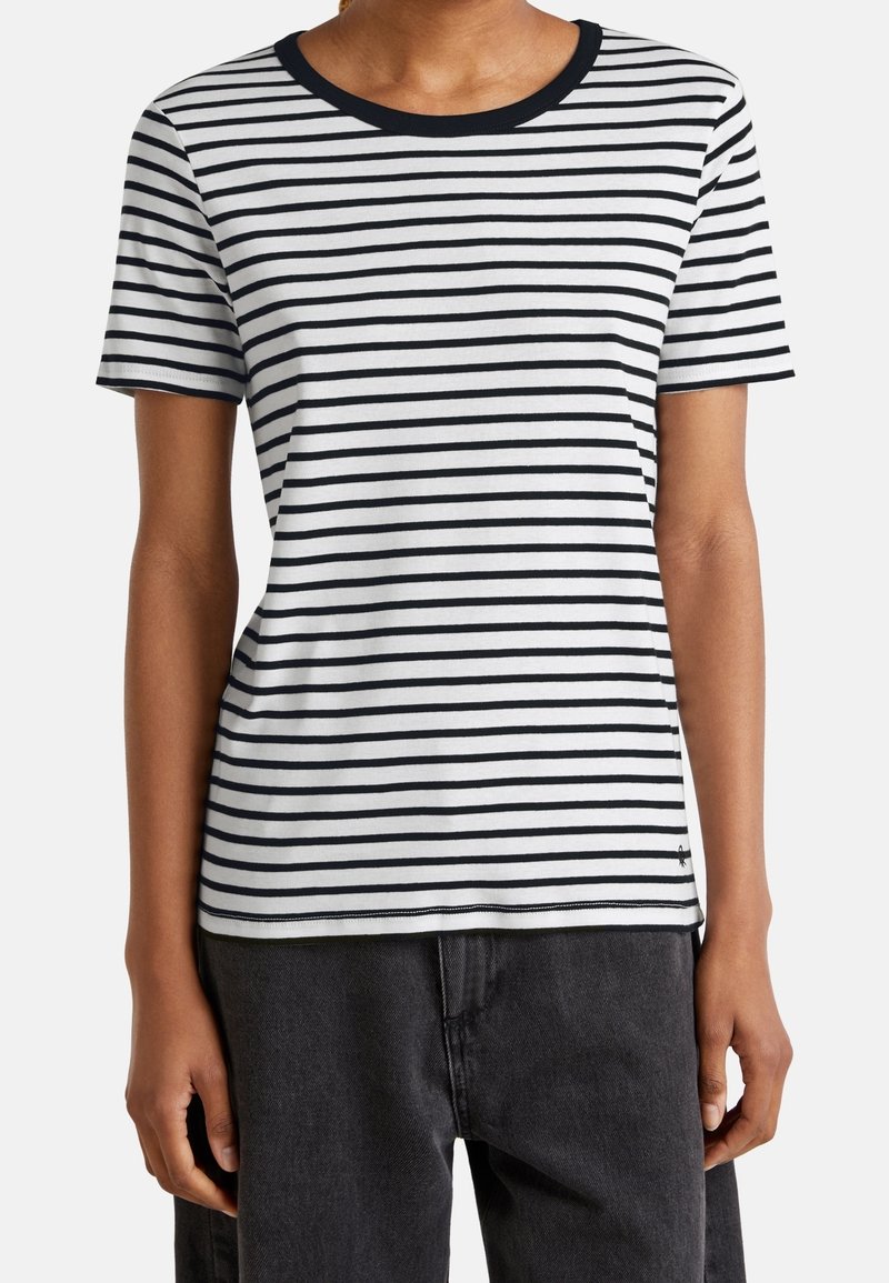 Vit kortärmad t-shirt med smala svarta ränder, svart rund halsringning och en subtil logotypdetalj nära fållen.