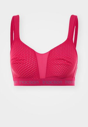 Red sports bra with a mesh design, featuring dotted texture and a breathable panel. Elastic band with "traction" branding along the bottom.