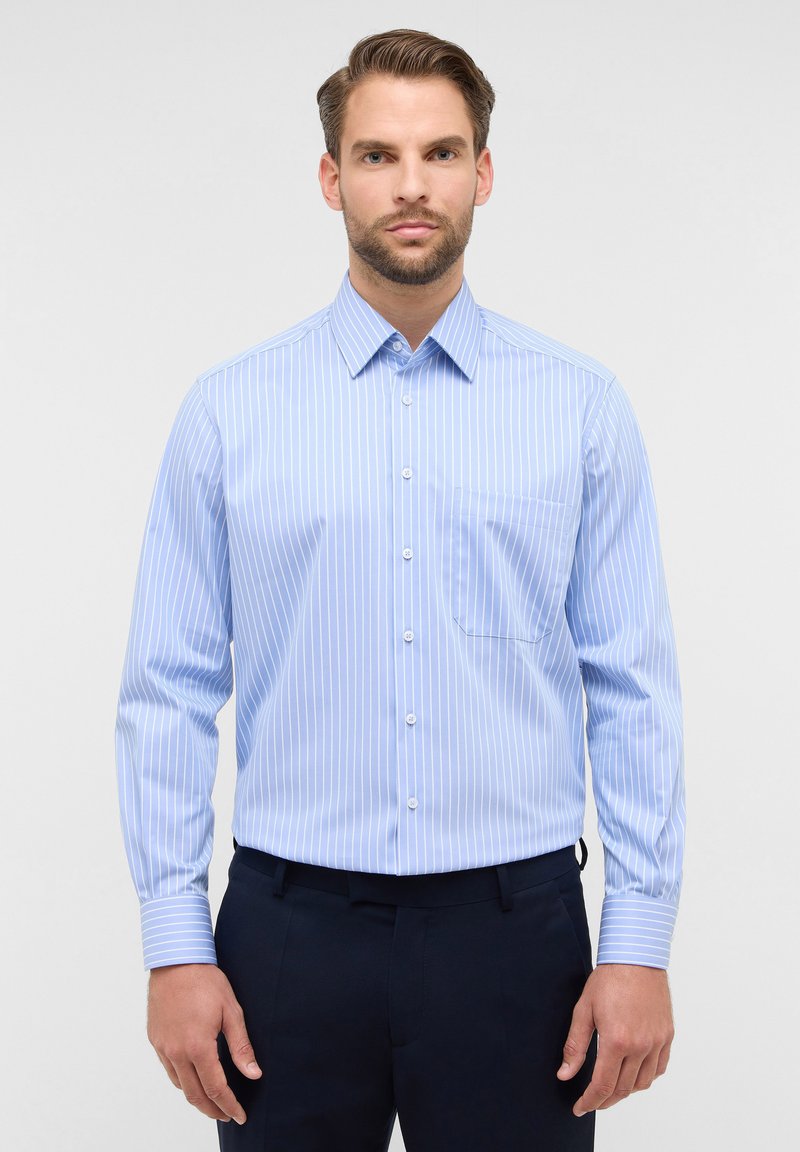 Camicia azzurro chiaro a maniche lunghe con righe verticali bianche, con bottoni davanti, colletto a punta e una tasca sul petto, abbinata a pantaloni scuri.