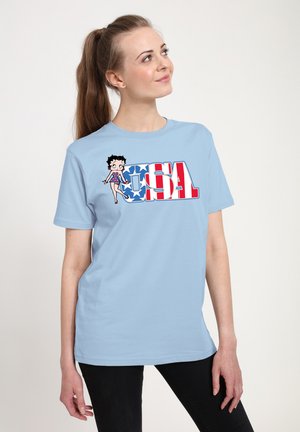 Lys blå bomulds t-shirt med et grafisk design, der viser en karakter og "USA" i rød, hvid og blå farver. Korte ærmer, afslappet pasform.