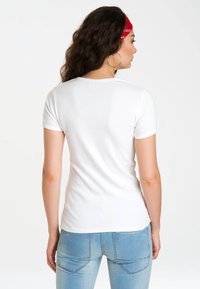 White short-sleeve t-shirt made of smooth fabric, fitted design, rounded neckline, and a slightly curved hem. Paired with light blue jeans.