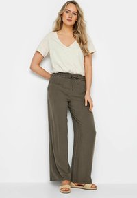 Lichtbeige V-hals t-shirt, losse fit. Olijfgroene wijde broek met een elastische tailleband en een verwisselbaar touwtje. Tan sandalen met een getextureerde strap.