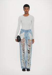 Top de mangais longas cinza claro combinado com jeans de denim azul claro desgastados, com grandes rasgos e bordas desfiadas, acessorizado com uma carteira preta.