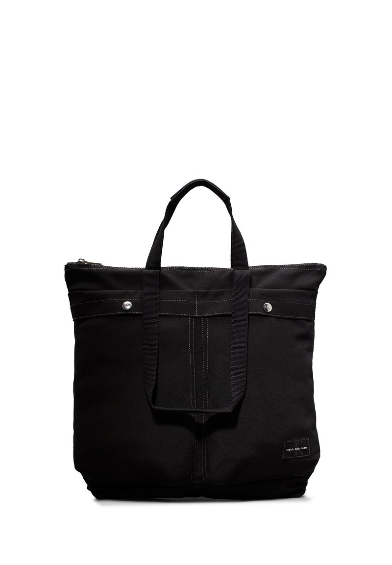 Svart stoff totebag med doble håndtak, glidelås og front sydd detalj. Har logo-patch og sølvfargede hardware-aksenter.