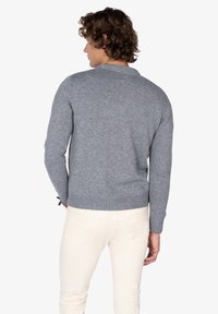 Suéter gris de punto con escote redondo y dobladillo acanalado, mostrado por la parte de atrás, combinado con pantalones de color claro.