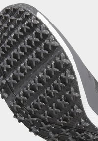 Svart atletisk skosula med multidirektionella klossar i ett korsmönster; inkluderar en vit kant längs kanten. Gummimaterial.