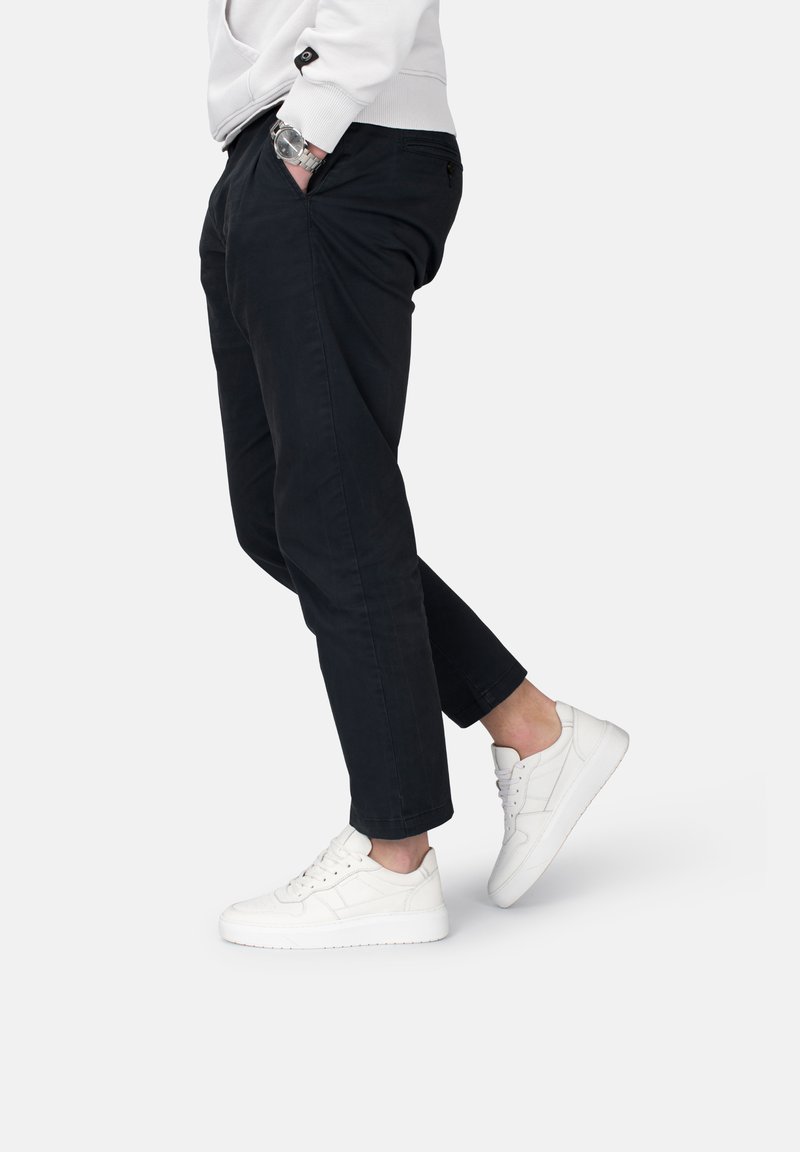Pantaloni scuri aderenti, abbinati a sneakers bianche. I pantaloni presentano tasche laterali e una texture liscia, mentre le sneakers hanno un design classico.