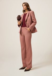 Dopasowana różowa marynarka na jeden guzik, w zestawieniu z dopasowanymi szerokimi spodniami i bordową bluzką. Do tego eleganckie, brązowe buty na szpilce.