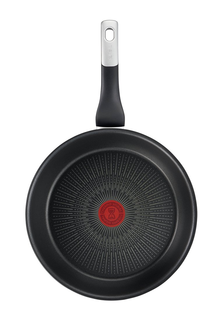 Schwarze antihaftbeschichtete Bratpfanne mit glatter Oberfläche, strahlenförmigem Muster, rotem Zentrum und einem Griff aus Edelstahl.