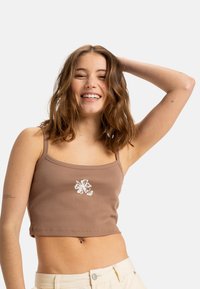 Bruine geribbelde crop top met dunne bandjes en witte bloemenborduursel op de voorkant. Glad textuur, strakke pasvorm en cropped lengte.