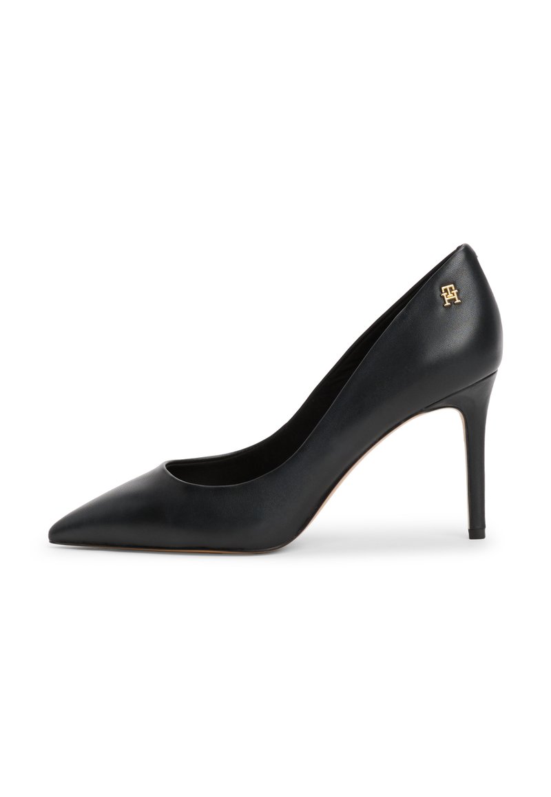 Musta nahkainen teräväkärkinen korkokenkä, jossa on stiletto-korko ja pieni kultainen logo-aksentti takakorkealla. Tasainen pinta ja tyylikäs muotoilu.