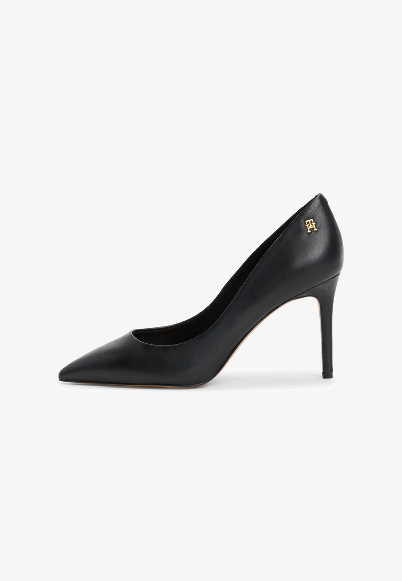 Pumps pretos de couro com bico fino e salto agulha, apresentando um pequeno detalhe em ouro no calcanhar. Textura suave com um design elegante.