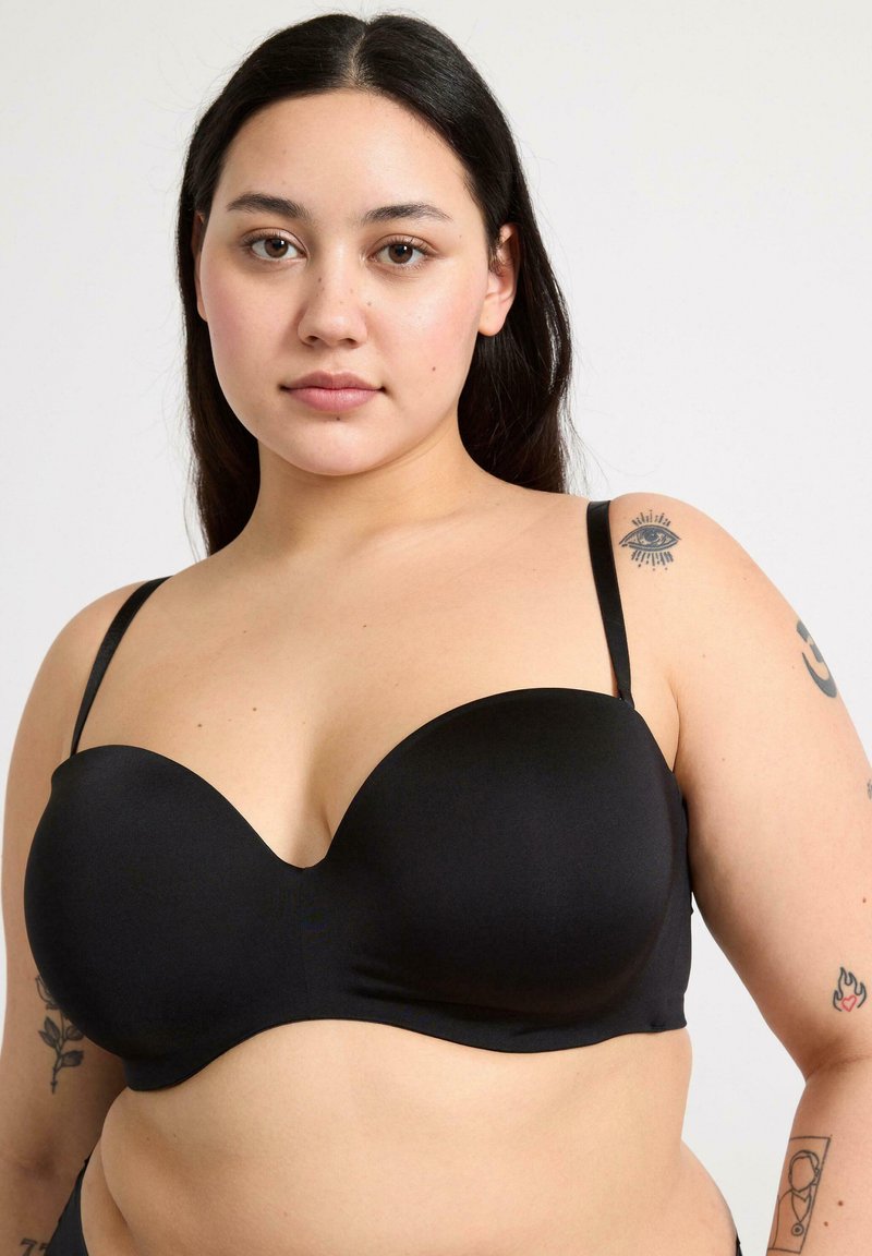 Le soutien-gorge noir présente un design lisse et moulé avec des bretelles réglables et un décolleté plongeant. Le matériau est élégant et extensible pour plus de confort.